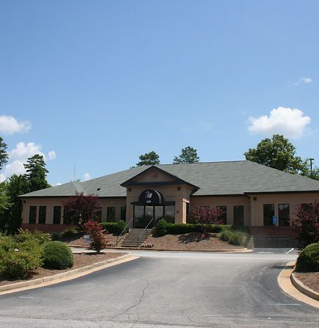 Single-story building with a central entrance, gray roof, and curved driveway under a clear blue sky