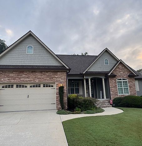 Suburban brick house with two-car garage, front porch, and manicured lawn at dusk
