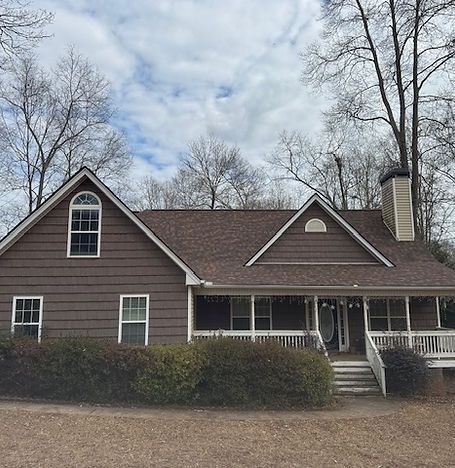 Brown house with a front porch, white trim, and leafless trees under a cloudy sky