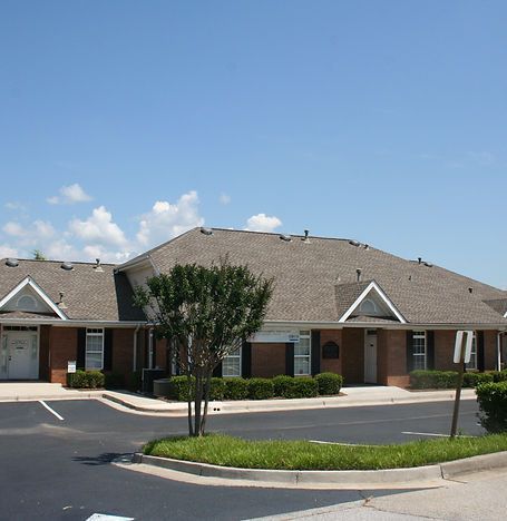 Single-story brick townhouse with a tan roof, small trees, and a paved driveway under a clear blue sky