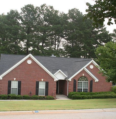 Brick suburban house with dark roof, black shutters, and arched window, fronted by a lawn and trees