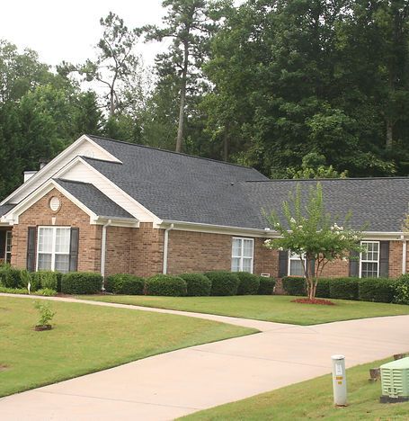Single-story brick house with gray roof, manicured lawn, and driveway in a suburban neighborhood