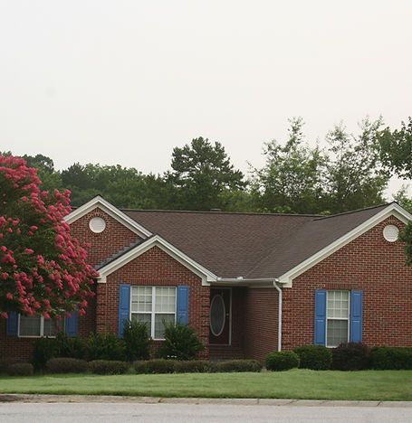 Single-story brick house with blue shutters, a red flowering tree, and a green lawn