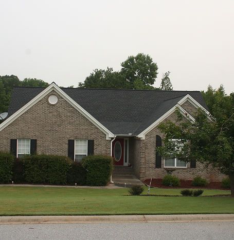 Single-story brick house with dark roof, white-trimmed windows, and manicured lawn on a quiet street
