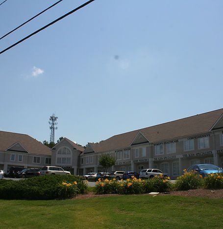 Row of beige motel-style buildings with parked cars and flower beds under a clear blue sky