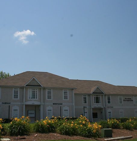 Two-story white building with brown roof behind yellow flowers under a clear blue sky