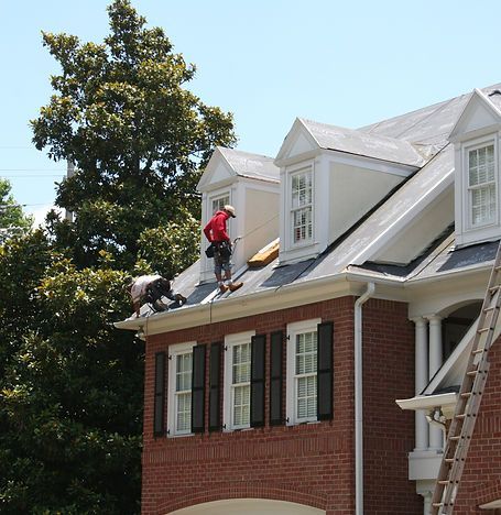 Workers repairing a brick house roof, with ladders and white dormer windows