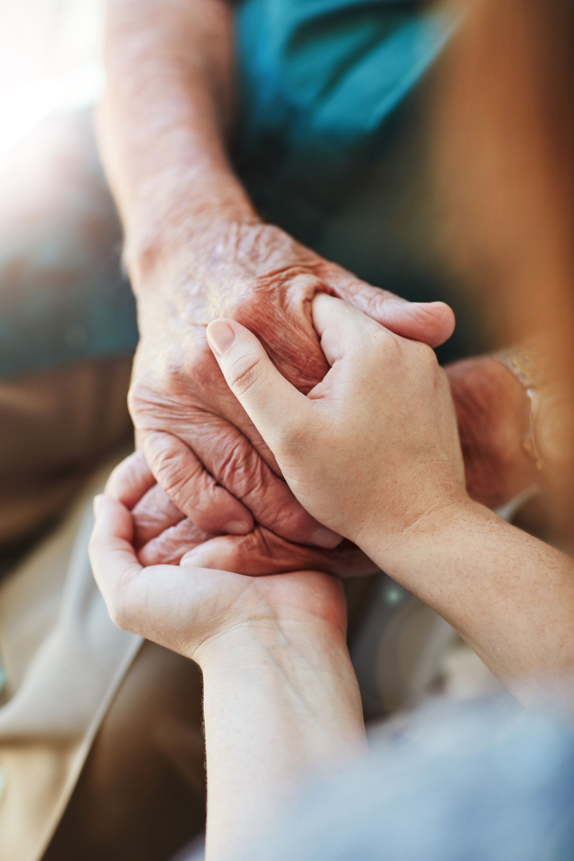 Hands gently holding an older person's hand in a warm, caring close-up.