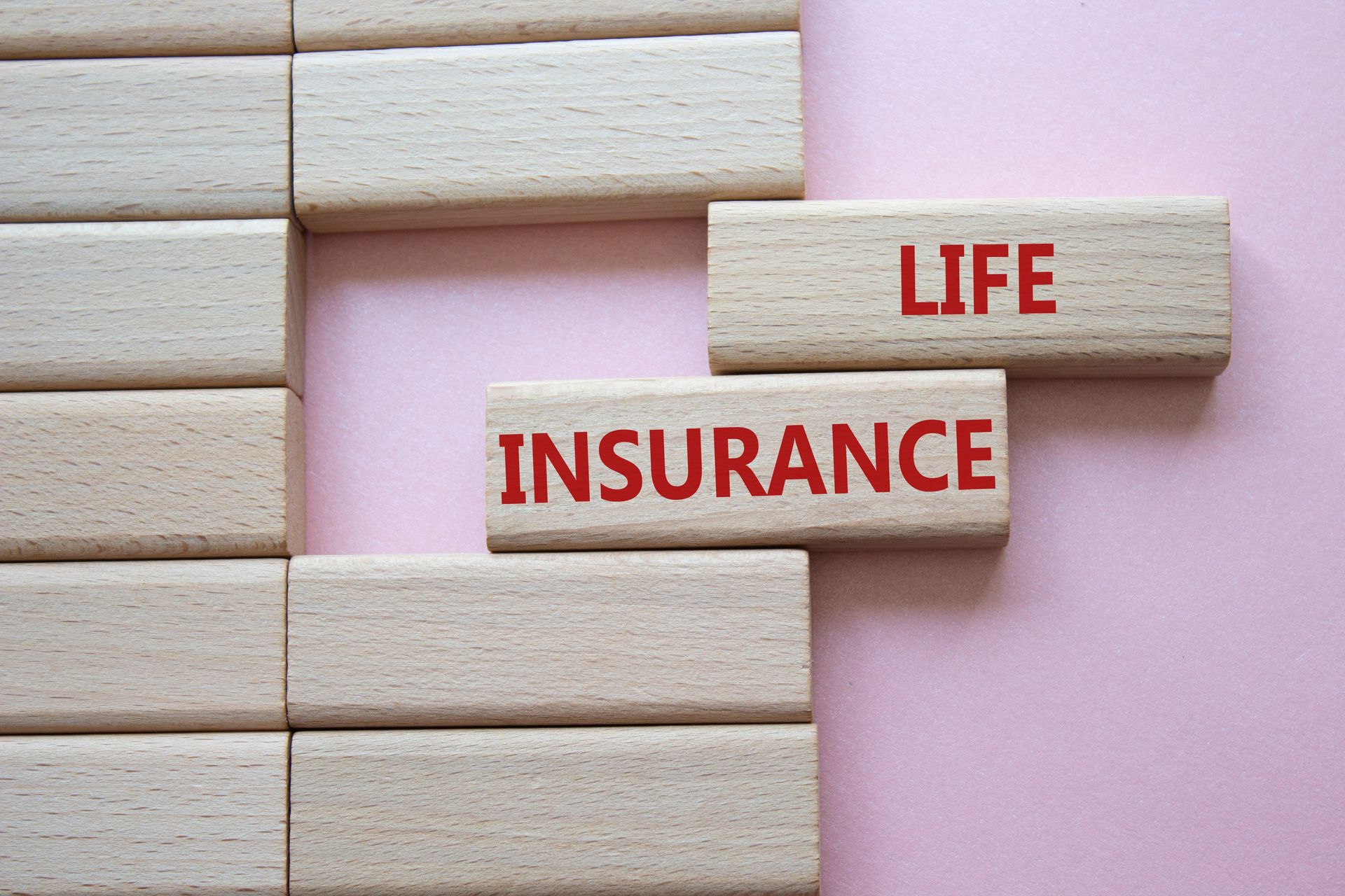 Wooden blocks on pink background spell “INSURANCE” and “LIFE” in red letters