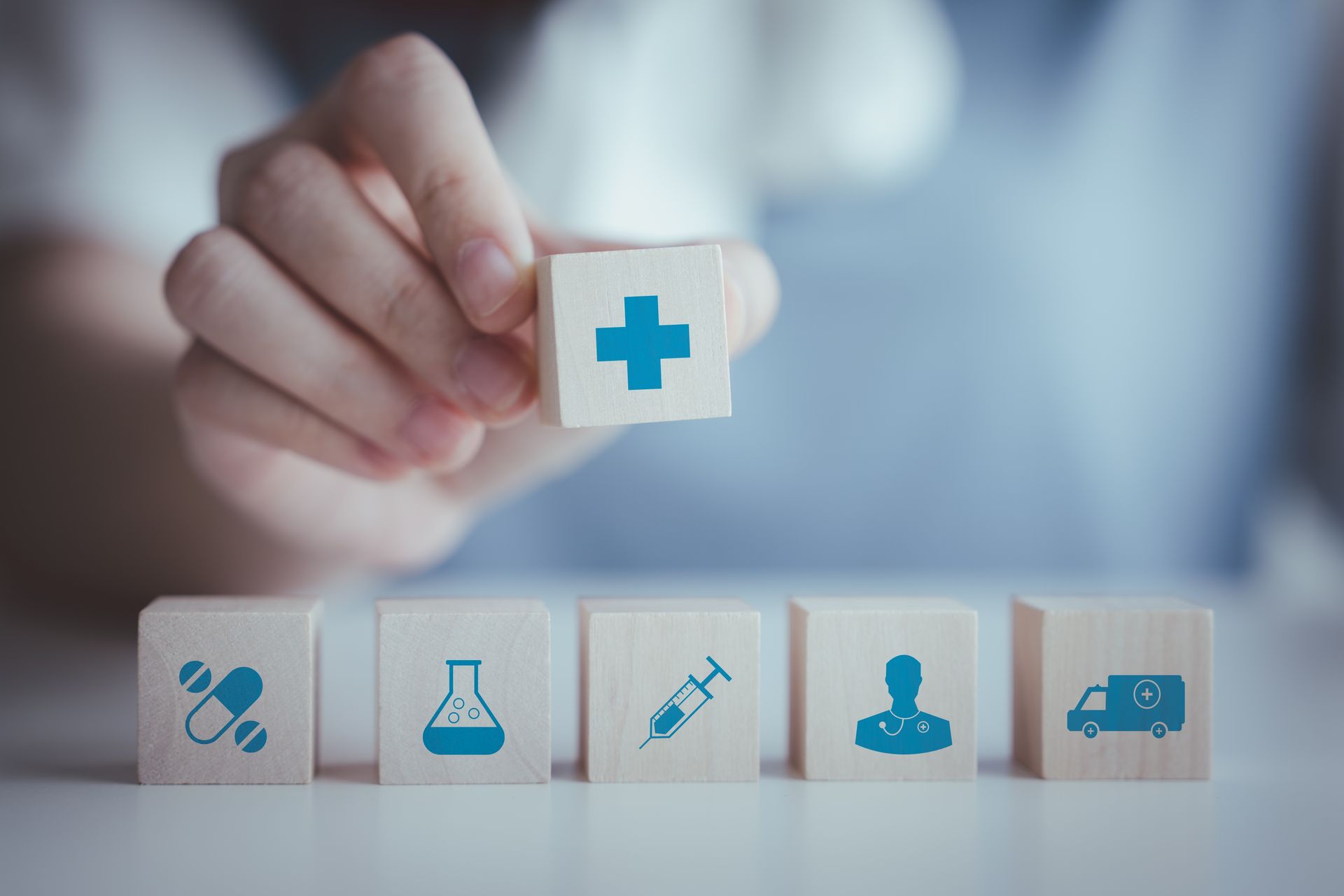 Hand placing a white medical block with a blue cross above health icon blocks
