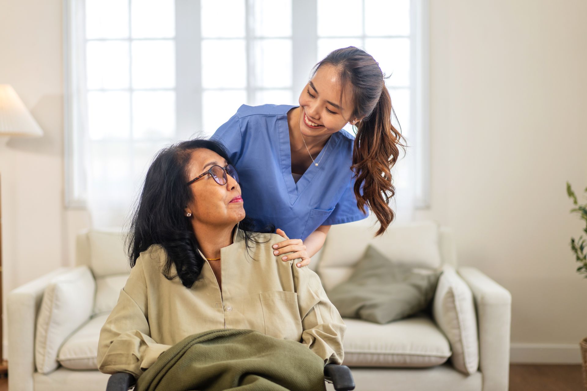 Two women in a bright living room, smiling and talking on a sofa.