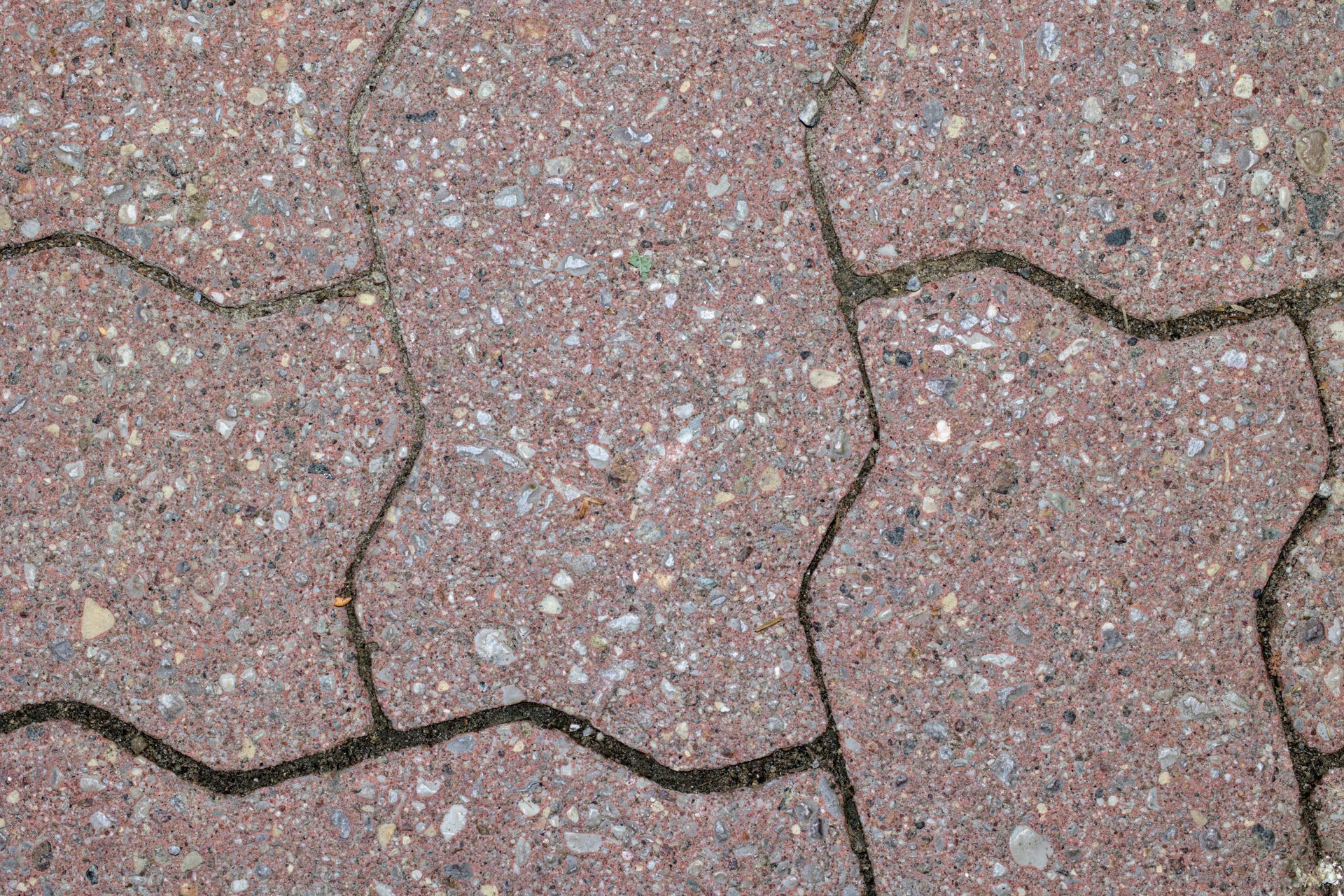 Cracked pink concrete pavement with dark gaps between tiles