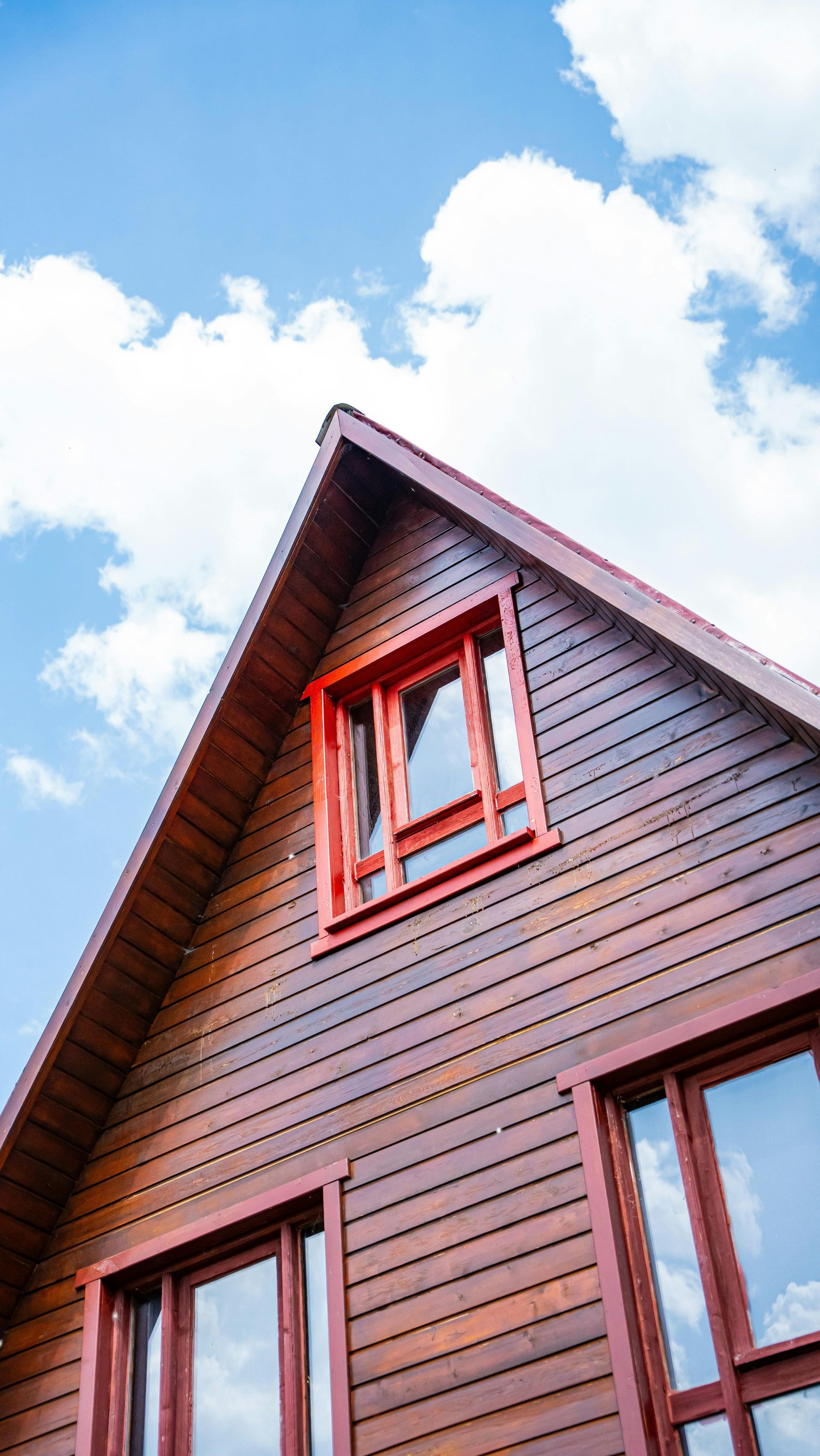 Red house exterior with steep roof and windows against a bright blue sky with clouds