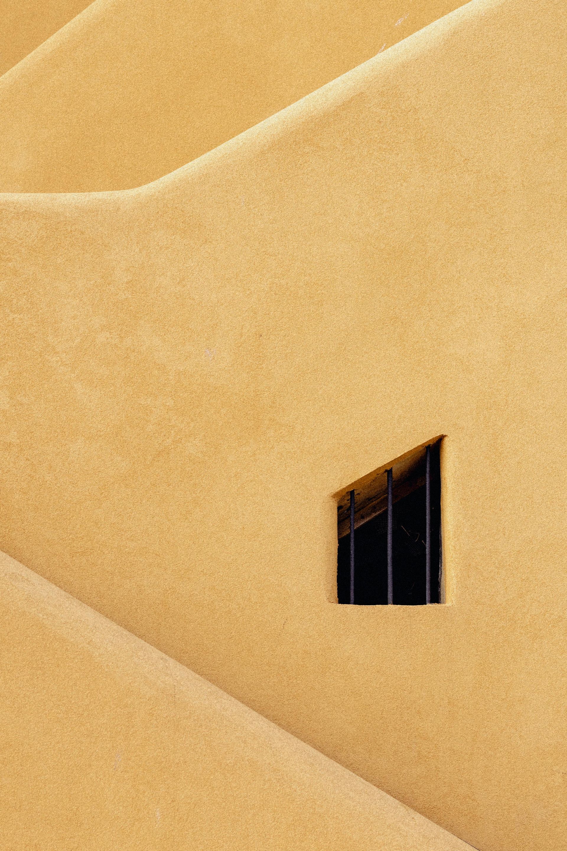 Golden sand dunes with a small dark window on a yellow wall or structure