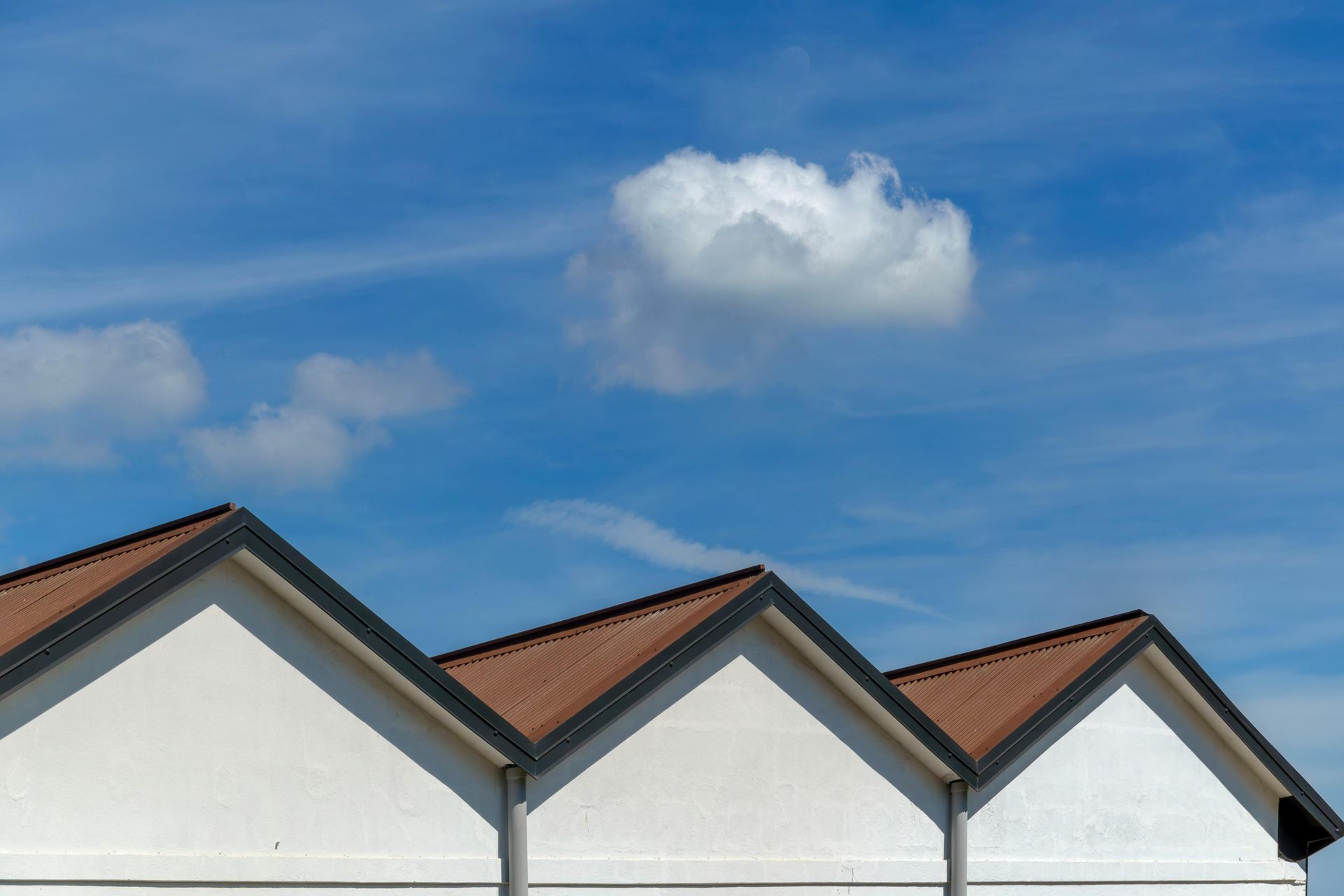 Three white house rooftops with red tiles beneath a blue sky and a single cloud