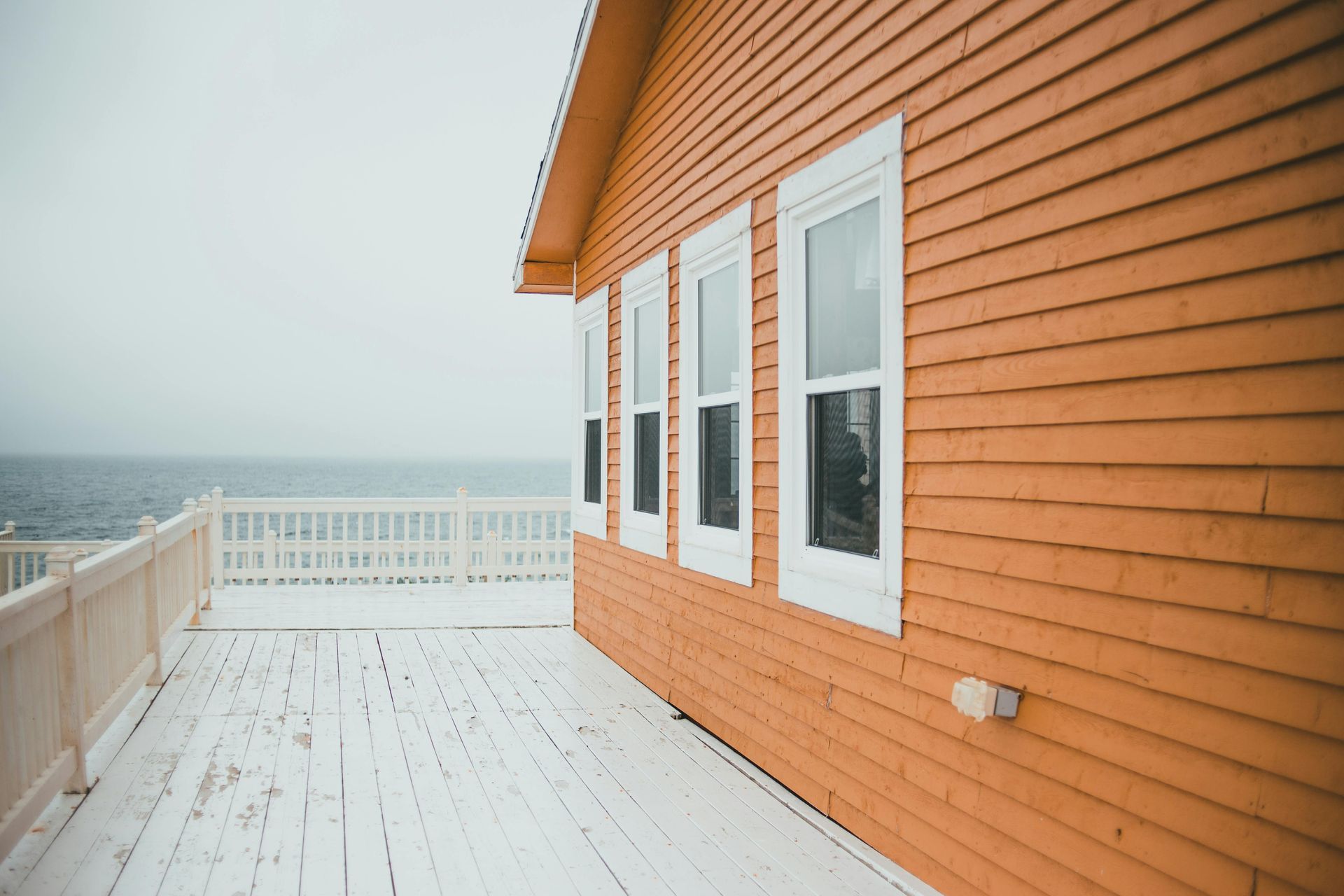 Orange-sided house with white deck overlooking the ocean on a cloudy day