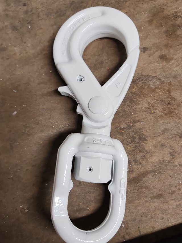 Mousqueton pivotant en métal blanc sur un sol marron.
