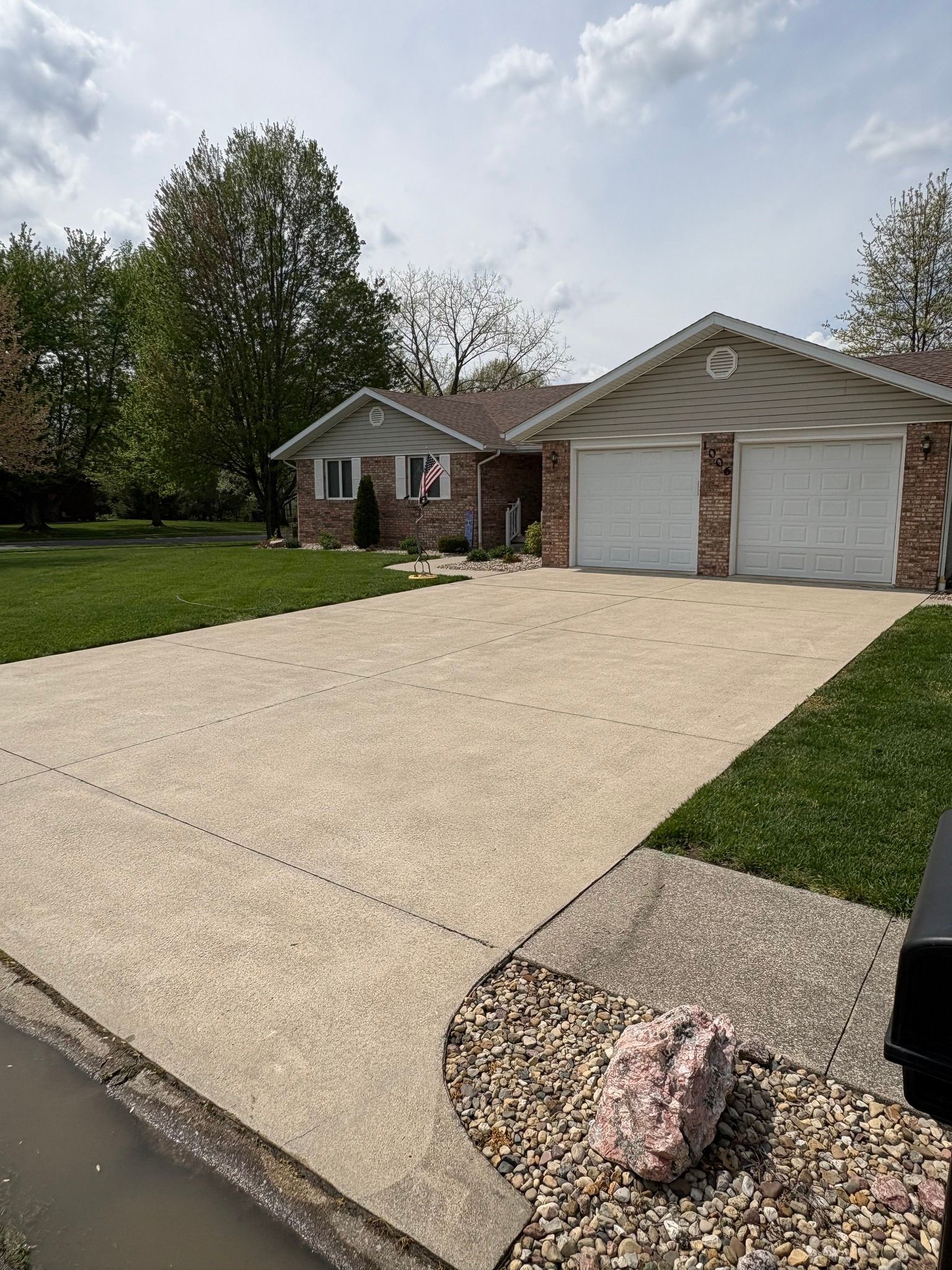 Single-story brick house with a double garage and wide concrete driveway beside a gravel rock bed.