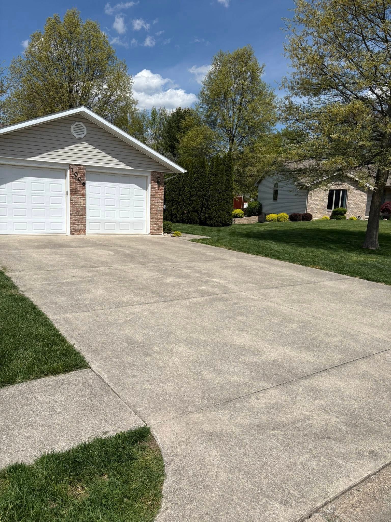 Suburban driveway leading to a white garage and house, with trees and green lawn under a blue sky.