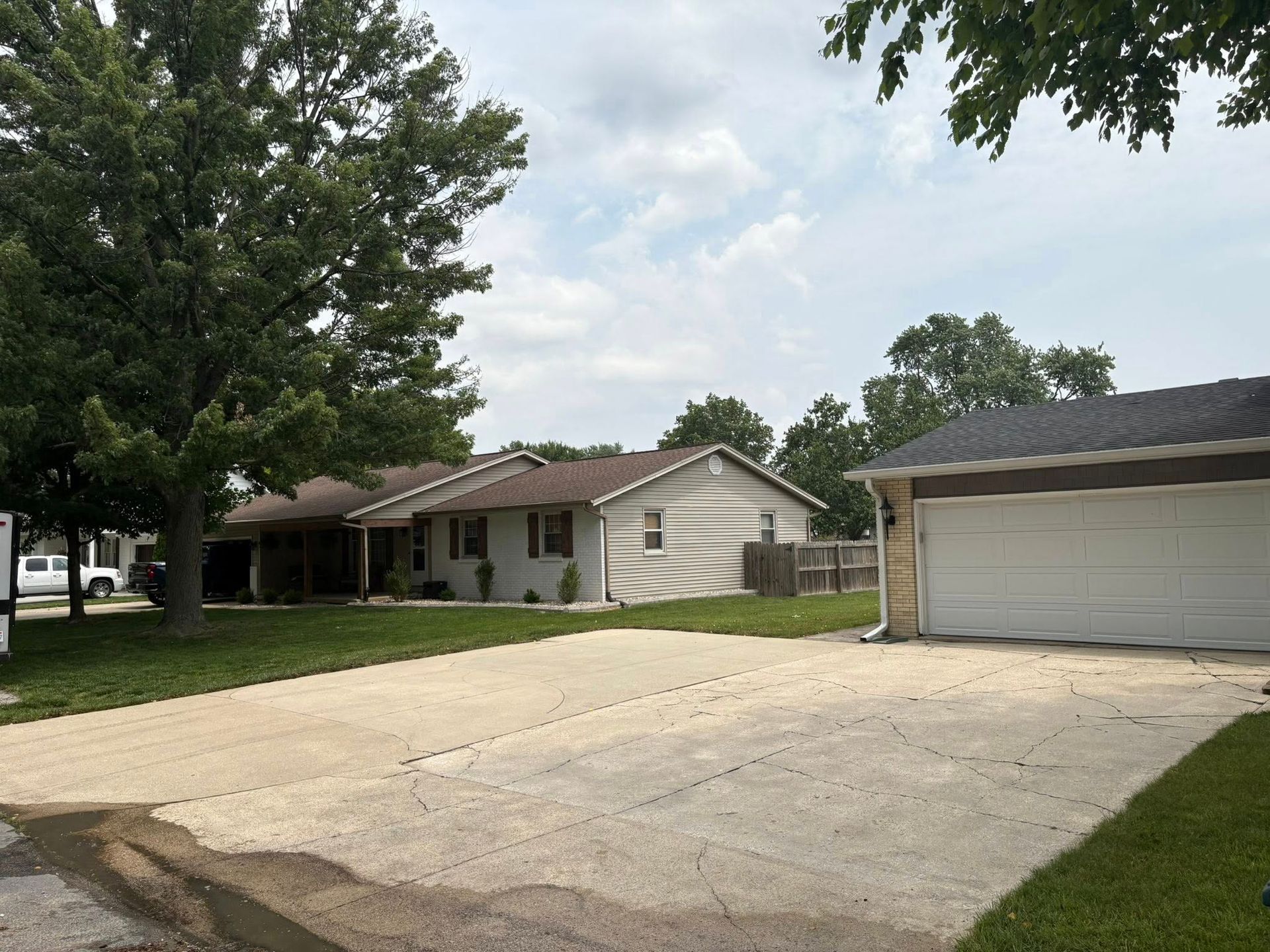 Single-story suburban house with a large driveway, attached garage, and trees in the yard