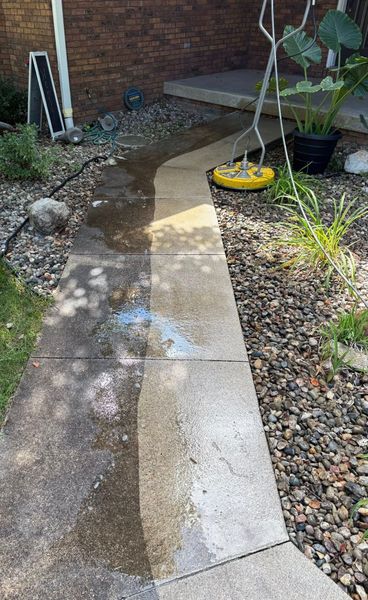 Concrete garden path with wet patch leading to steps beside a brick wall and gravel border