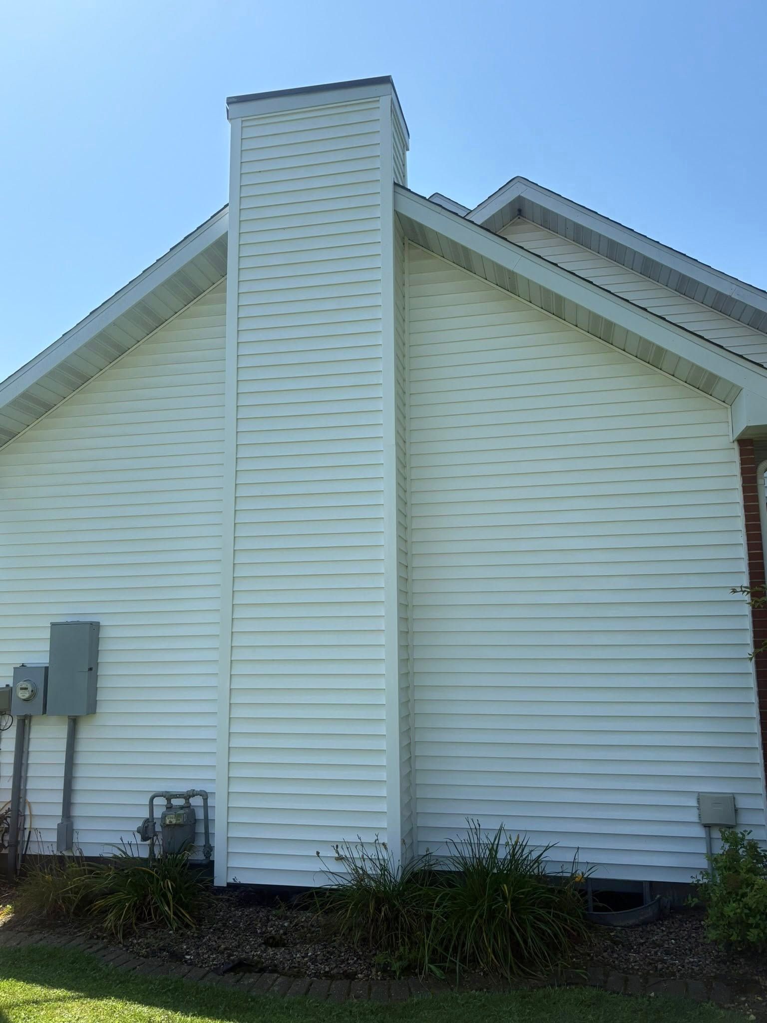 White house exterior with a central chimney and utility boxes on the side, under a blue sky