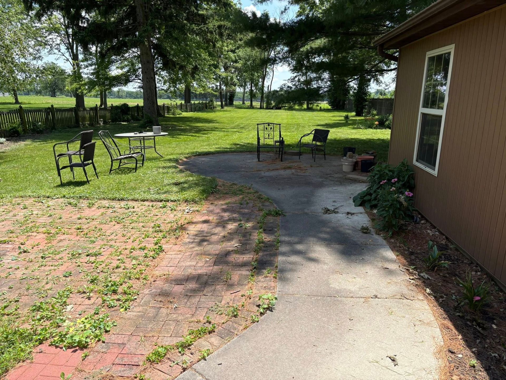 Backyard patio with chairs, tables, and a curved concrete path beside a brick house.