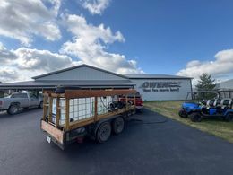 Flatbed trailer with stacked white panels parked outside a metal building under a blue sky.