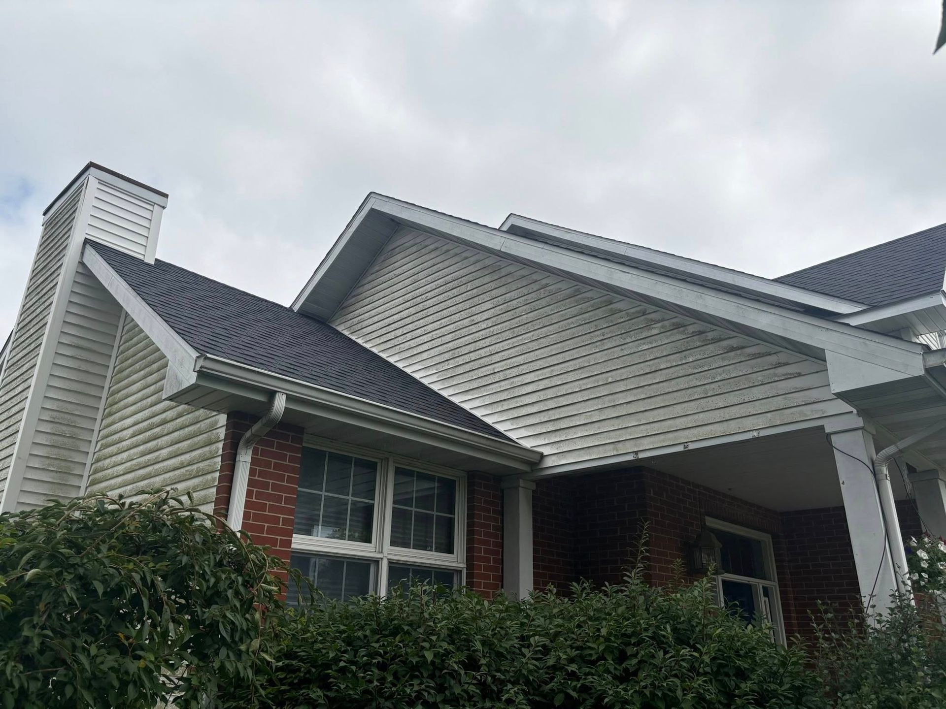 Suburban house exterior with gray siding, brick accents, and a covered front porch