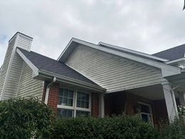 Suburban house exterior with gray siding, white trim, brick accents, and a gabled roof.