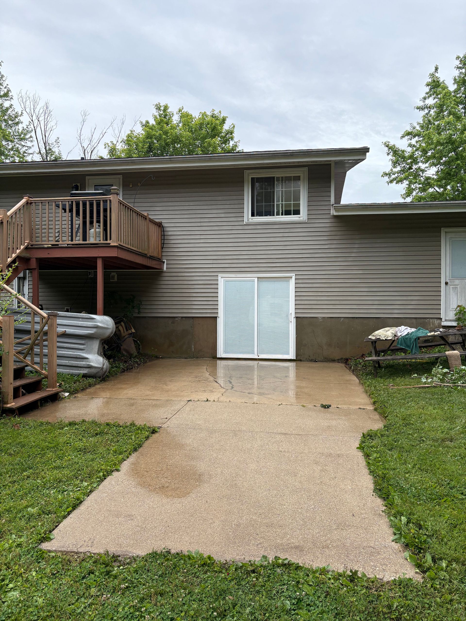Backyard view of a house with a small deck, concrete patio, and sliding glass door