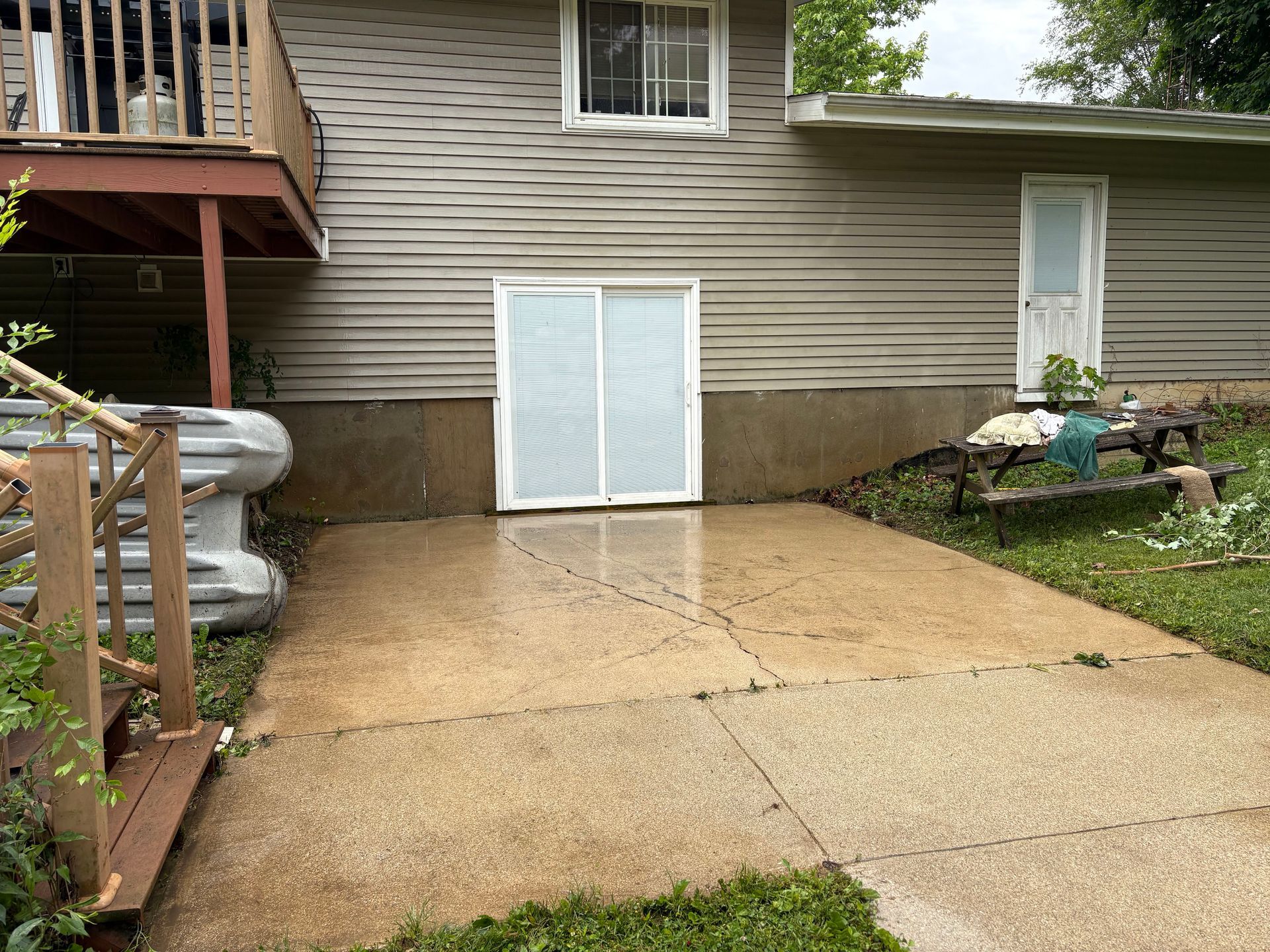 Rainy backyard patio with concrete slab, white doors, and steps beside a house