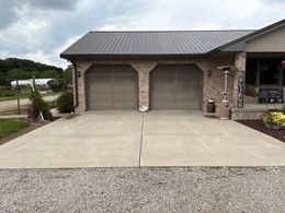 Two-car garage with stone exterior, concrete driveway, and gravel foreground under an overcast sky
