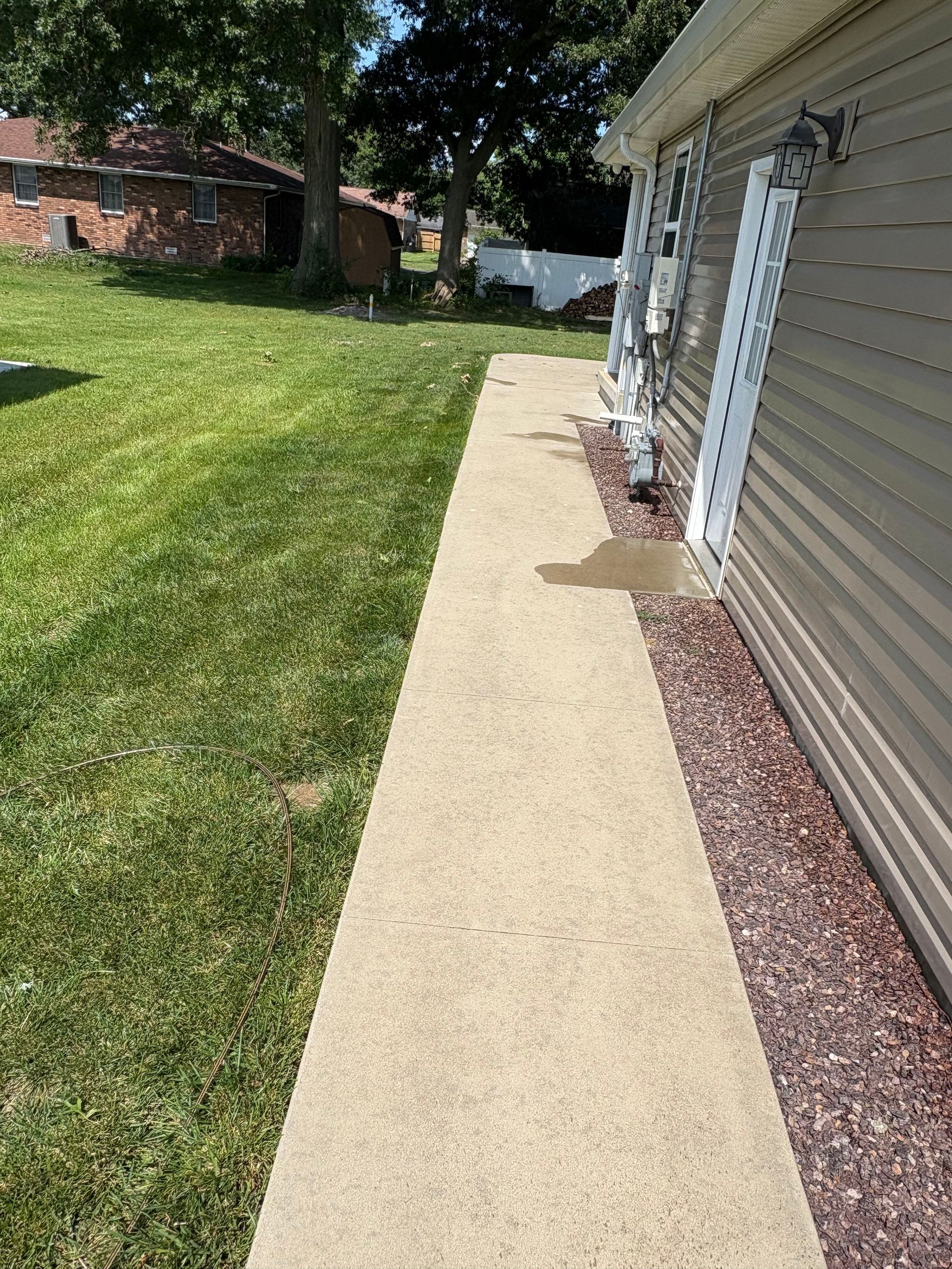 Concrete walkway beside a beige house and green lawn on a sunny day