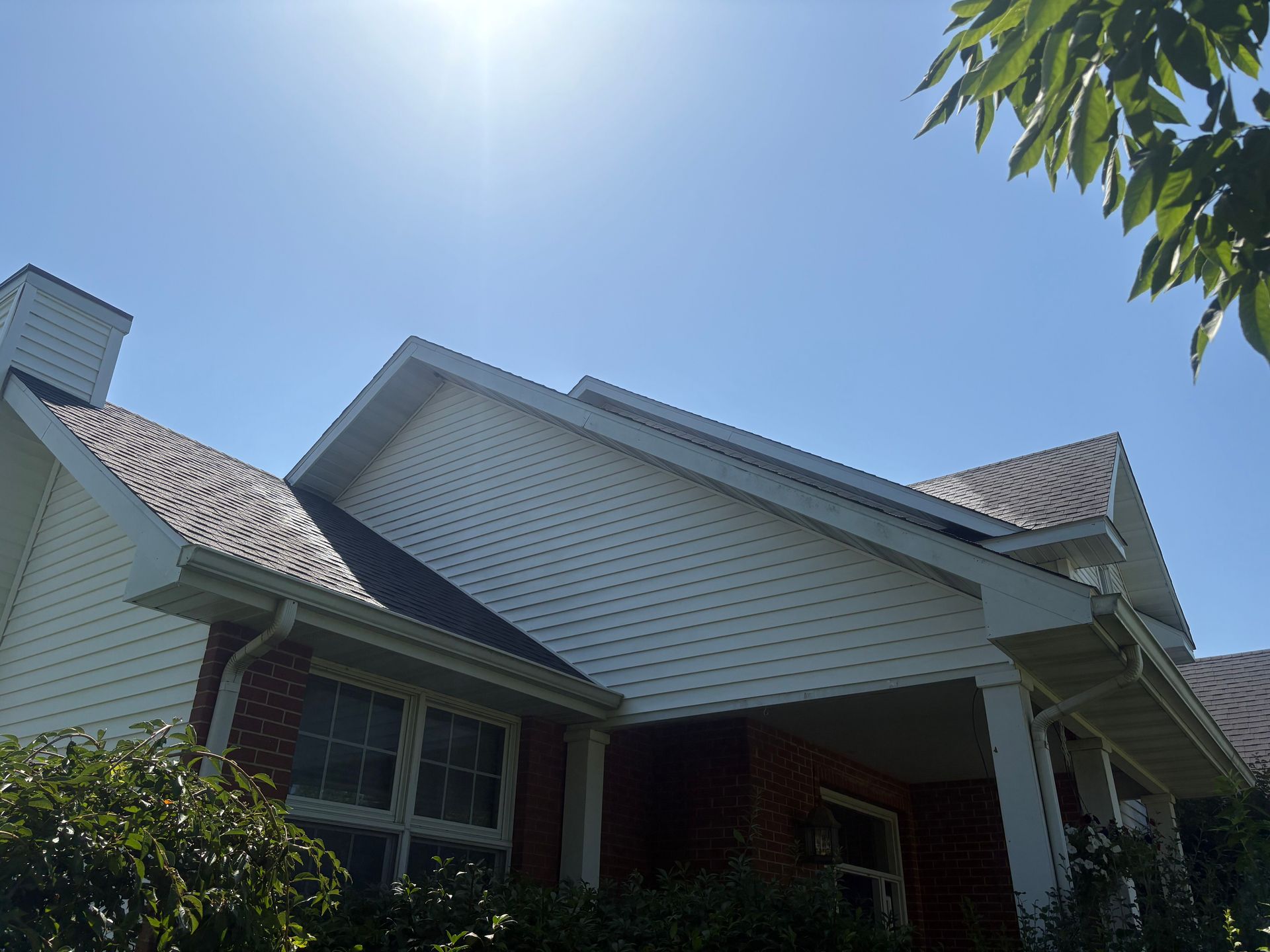 Suburban house with white siding and a red brick entry, seen under a bright blue sky
