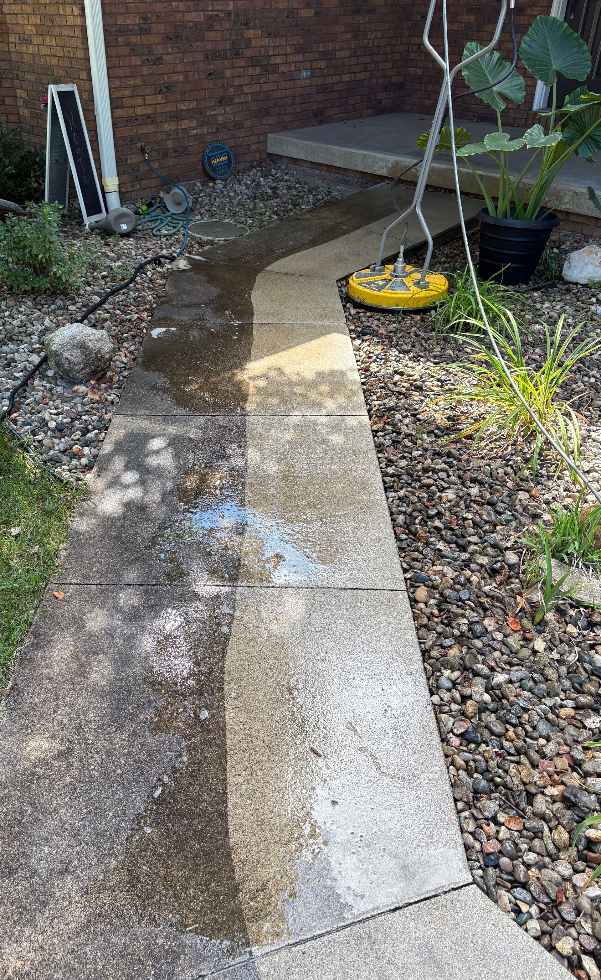 Wet stone garden path curving past gravel beds to a brick house entrance