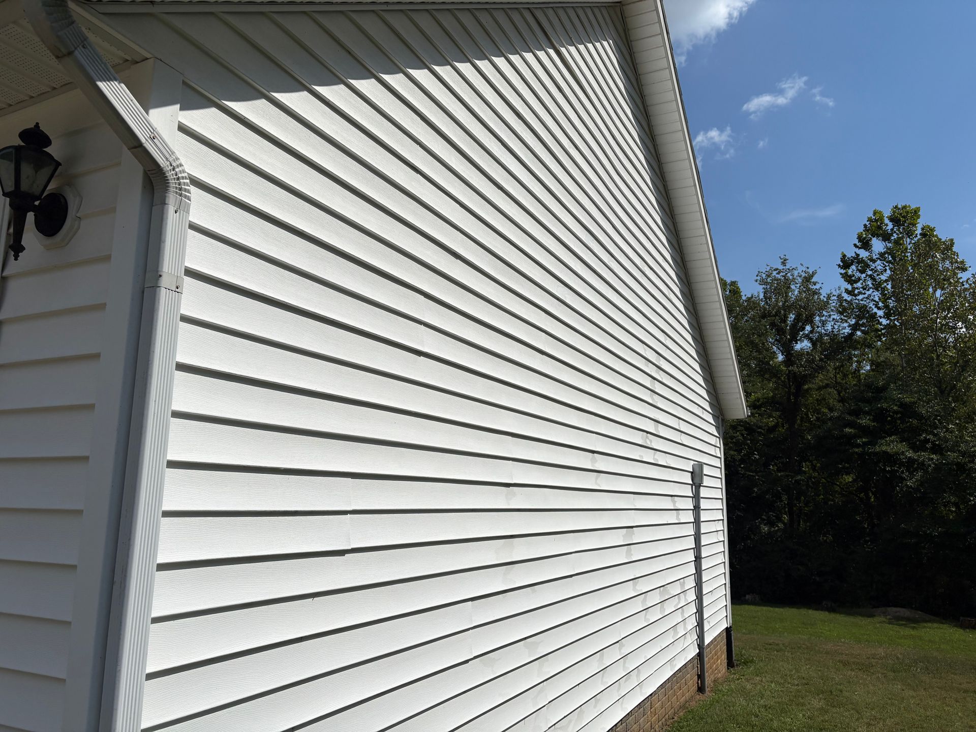 White vinyl house siding with a side wall, window trim, and grassy yard under a blue sky.