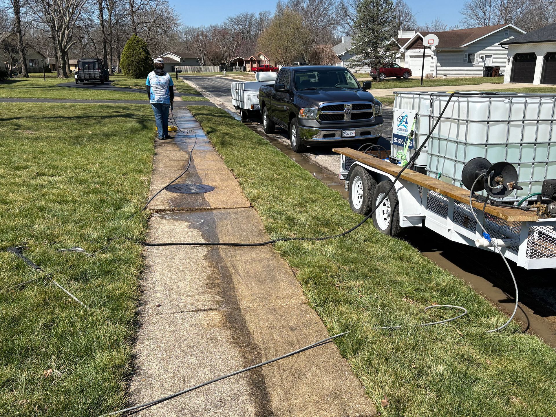Worker on a grassy roadside pulling a long cable beside parked utility trucks and trailers