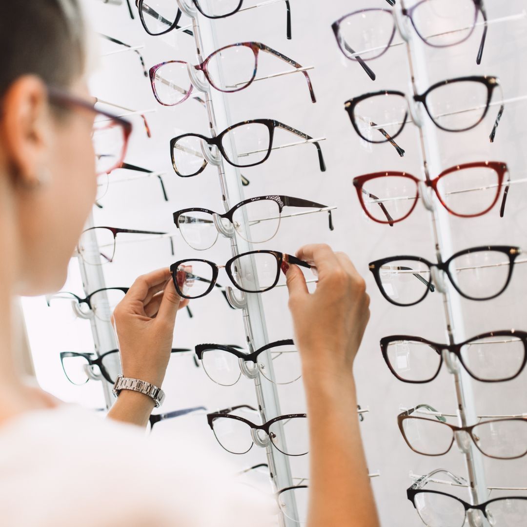 Woman selecting eyeglasses from a display rack in an optician's office.— EyeMax EyeCare in Wallsend, NSW