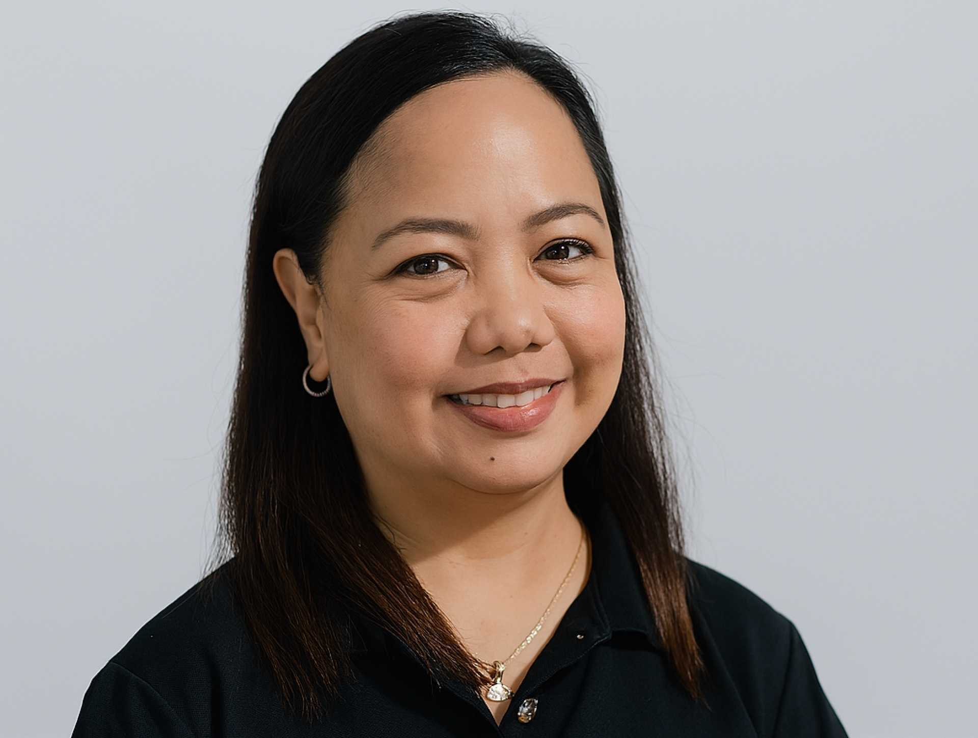 Woman with dark hair and a slight smile, wearing a black shirt, against a plain gray background.