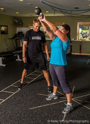 A man and a woman are lifting a kettlebell in a gym.