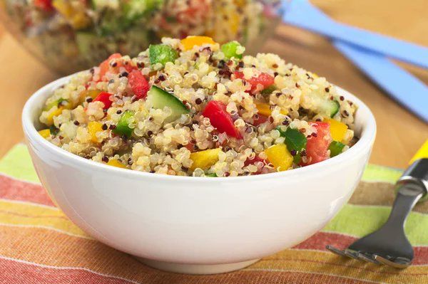 A bowl of quinoa salad with vegetables and a fork on a table.