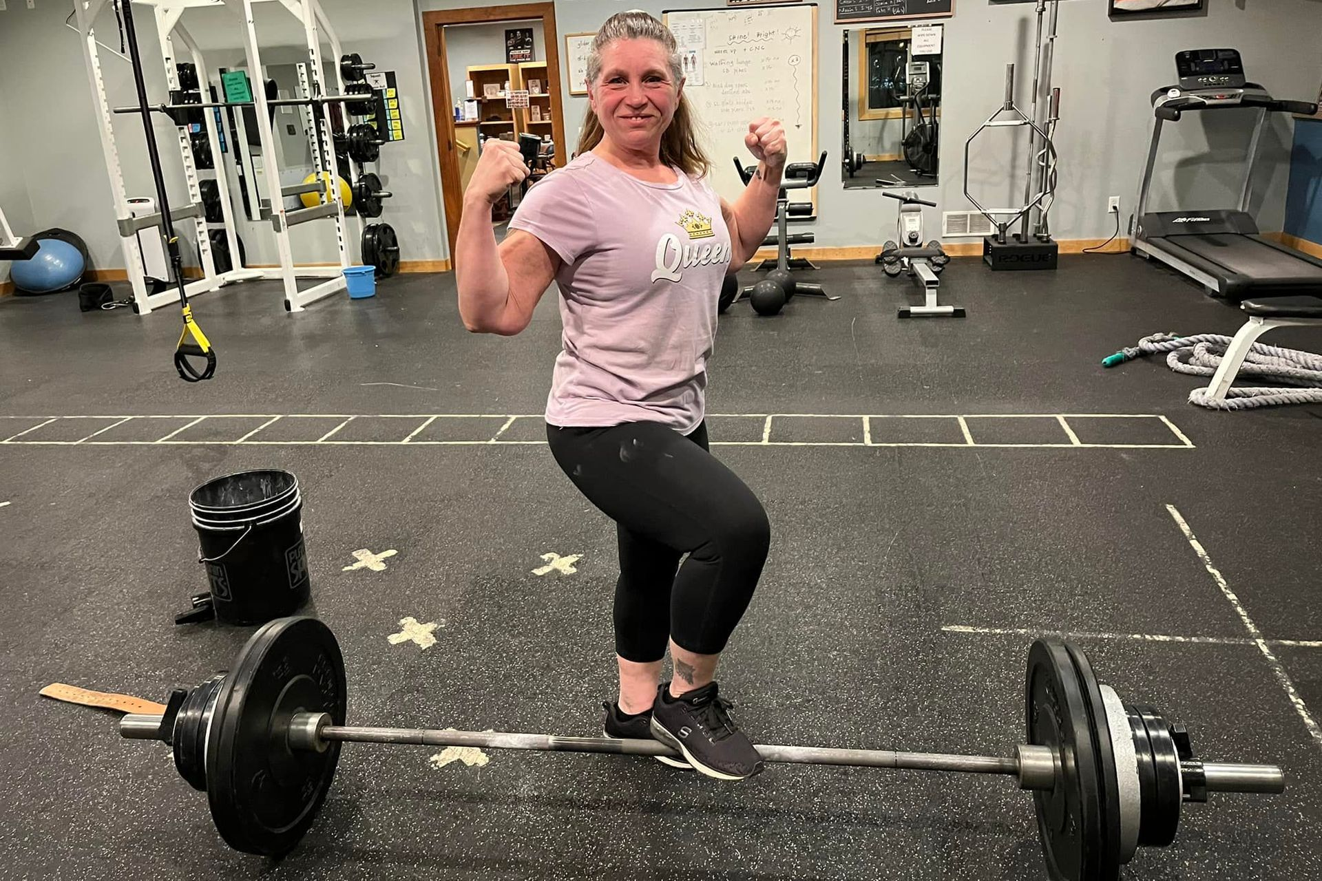 A woman is standing on a barbell in a gym.