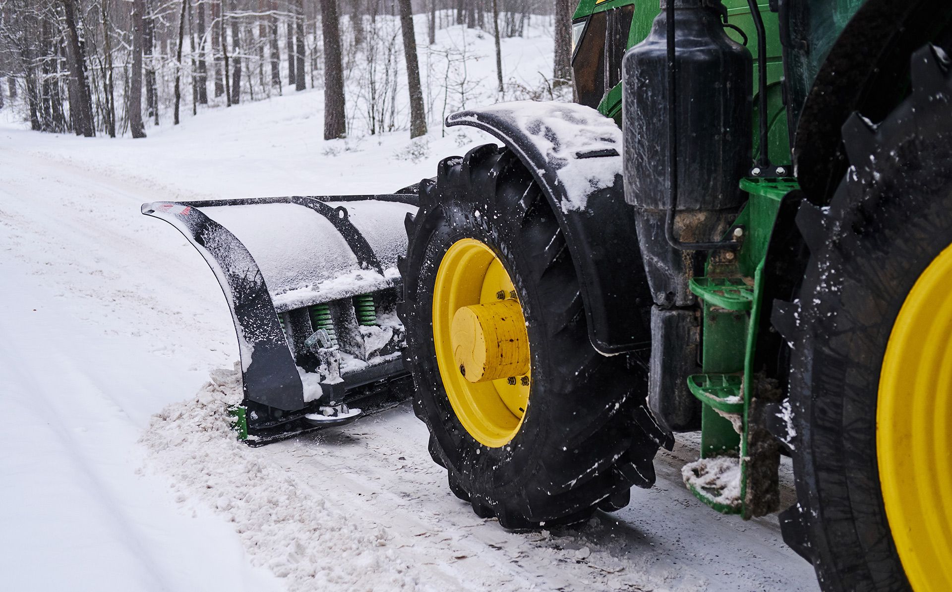 Green tractor plowing snow on a road; winter scene.