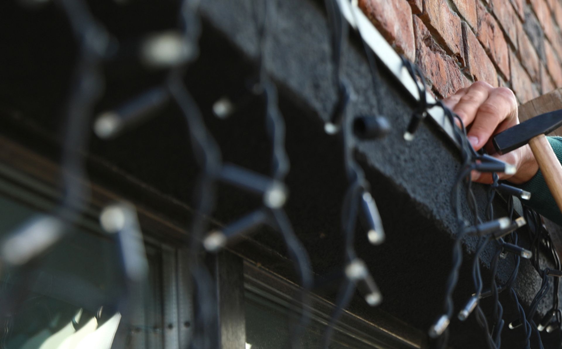 Person hammering Christmas lights onto a building's roof edge.