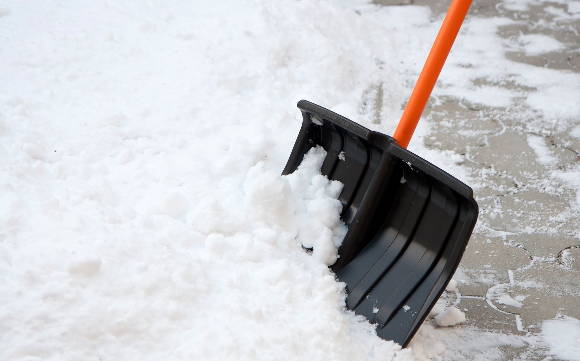 Black snow shovel with orange handle in snow.
