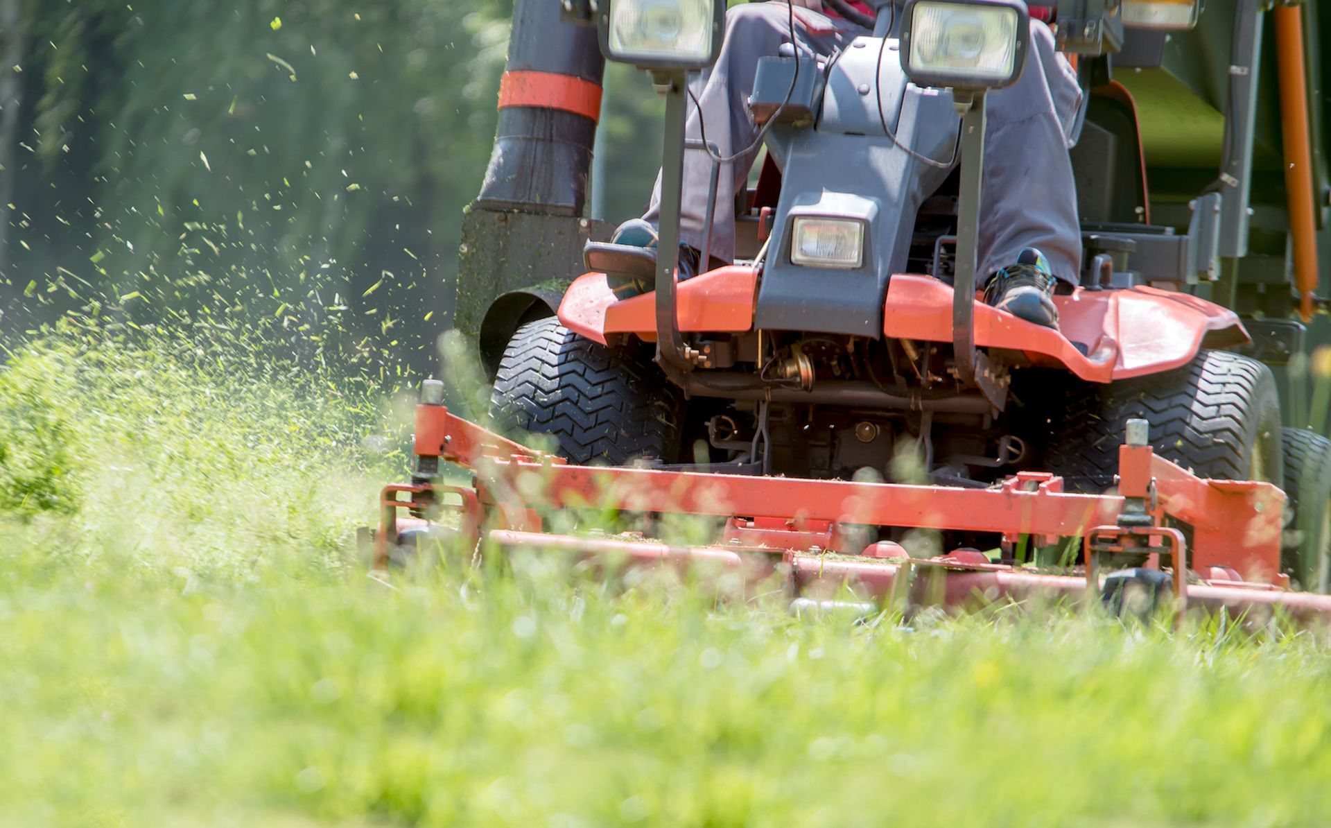 Orange tractor mowing green grass, blades visible.