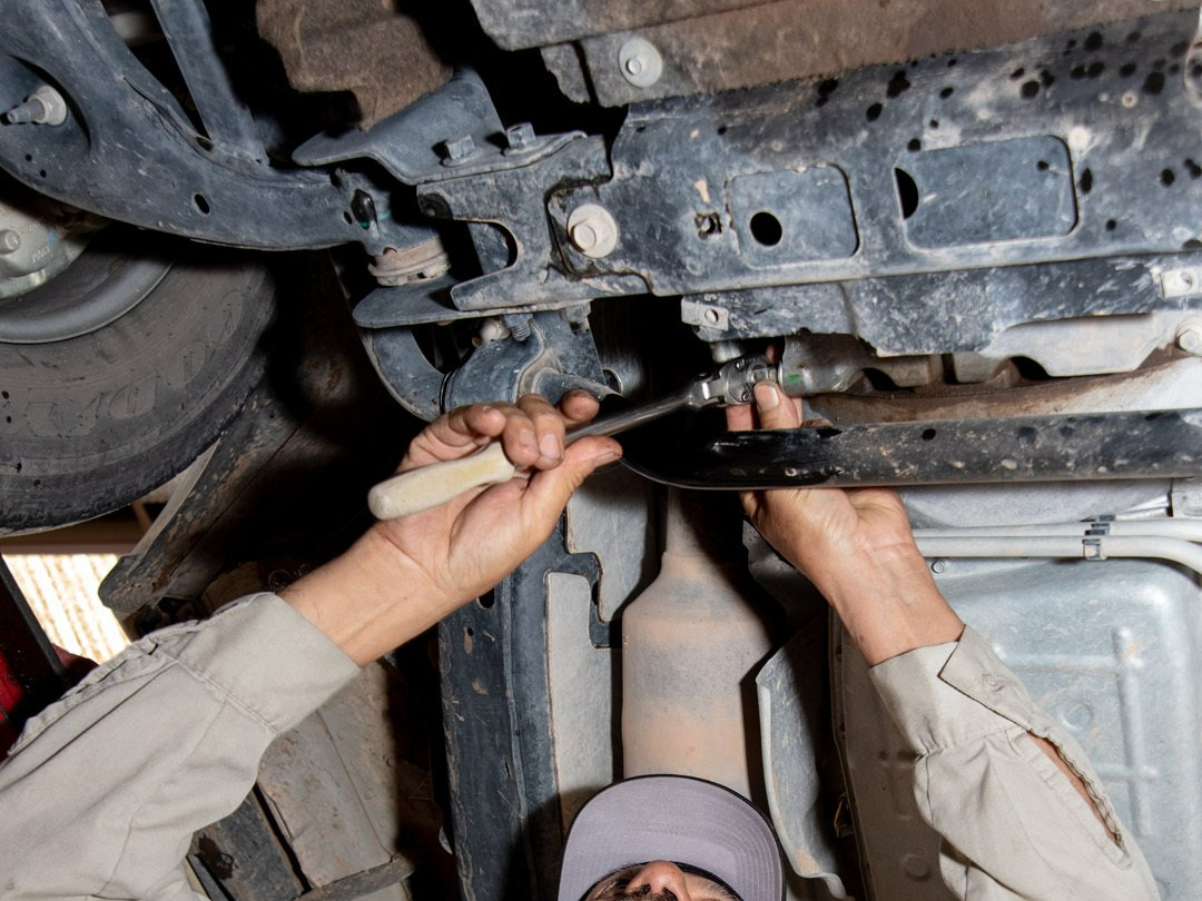 Mechanic working under a car, using a wrench on the undercarriage.
