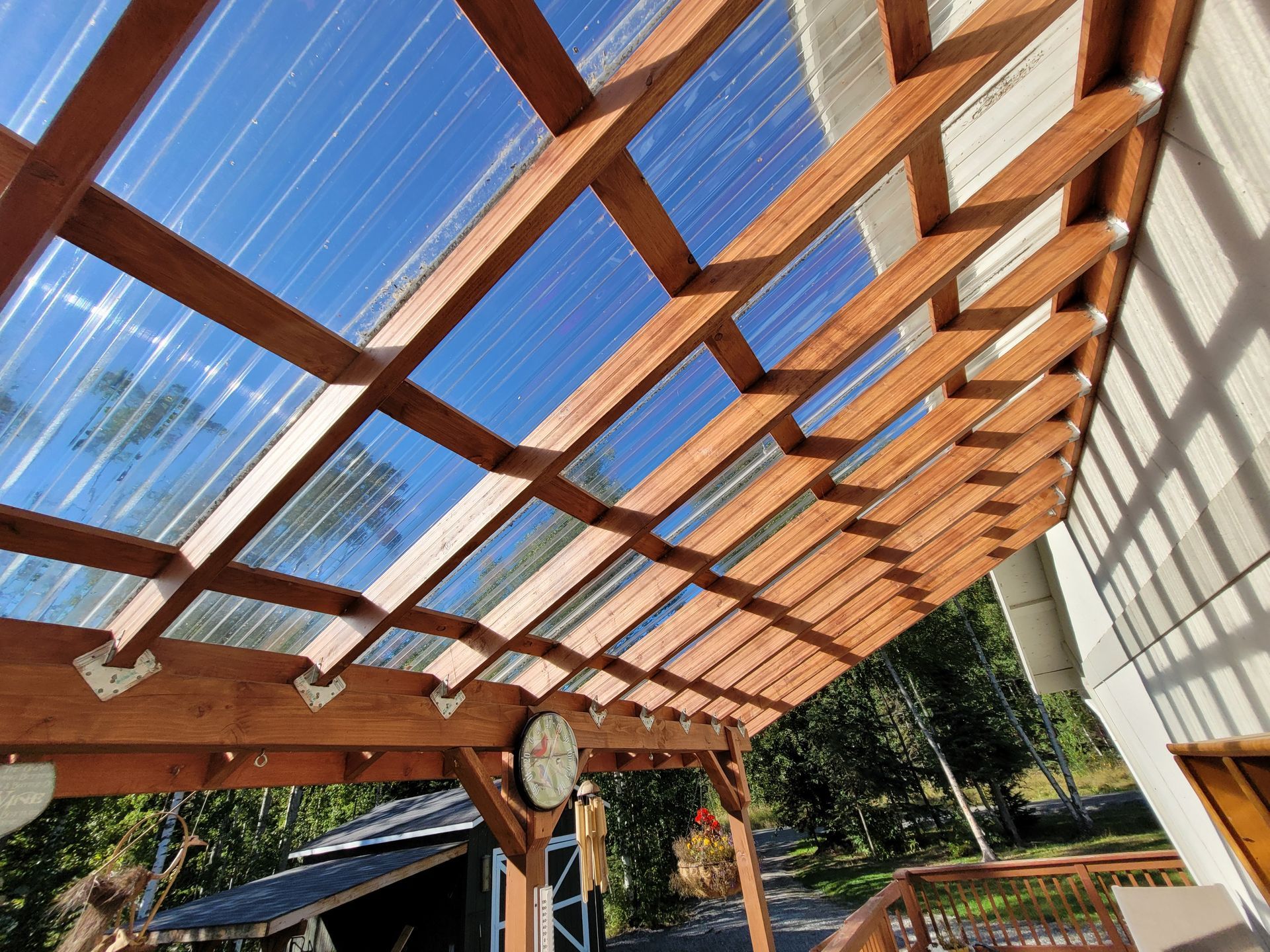 Wooden pergola with clear roof panels and blue sky overhead in an outdoor patio area