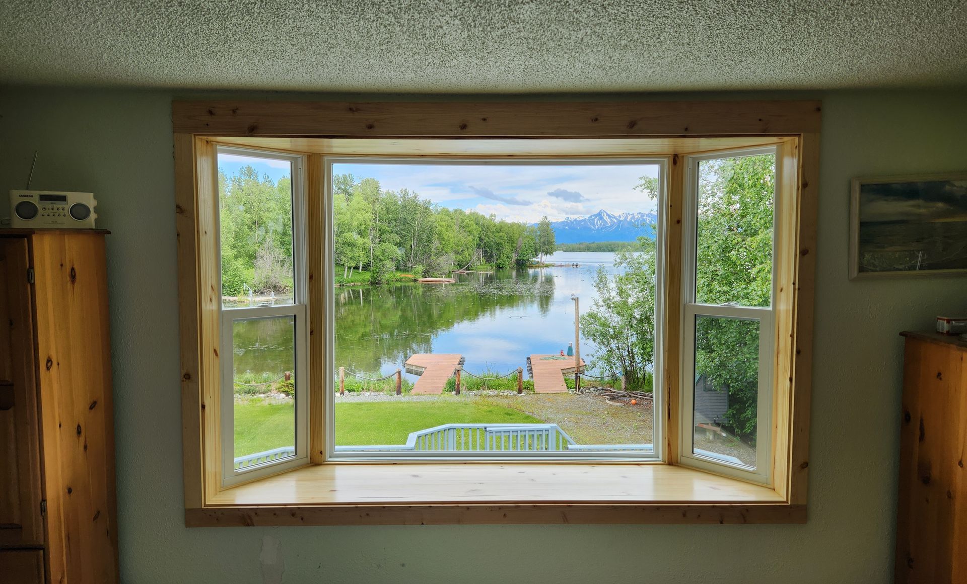 Open window framing a bright lake and trees, with a sunny blue sky beyond.